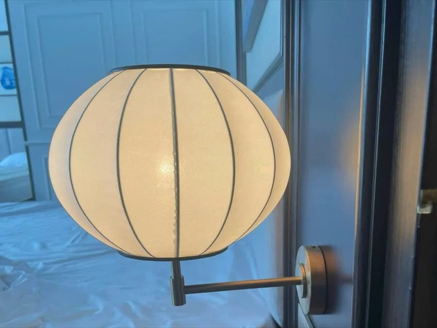 A round fabric wall light mounted at the bedside, built by KAHA