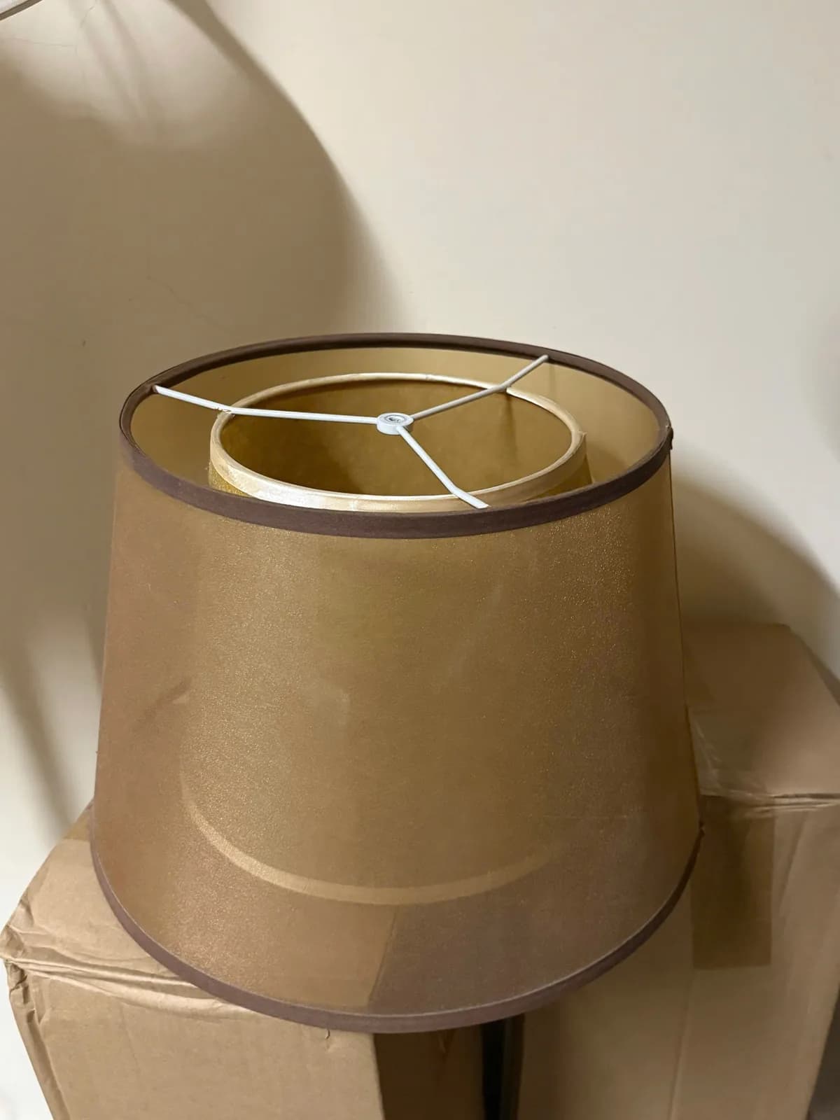 Chụp đèn vải vàng đặt trên thùng carton, nhìn từ trên xuống thấy vòng đỡ ba chân màu trắng
