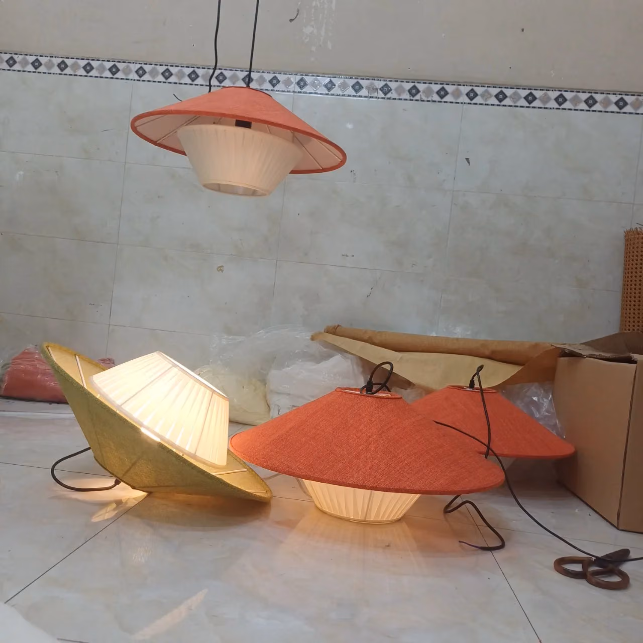 Đèn dáng nón bọc vải màu hồng và vàng đặt trên sàn